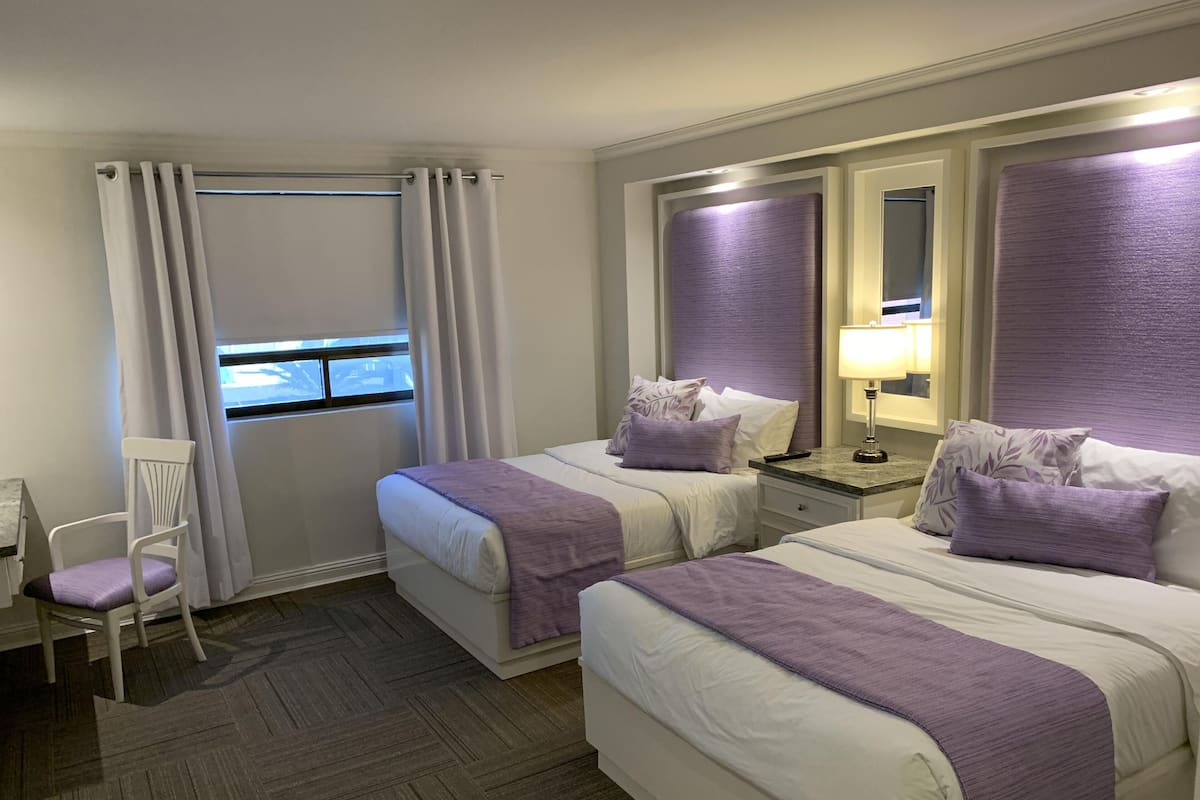 Une chambre d’hôtel avec deux lits, une chaise, une table de chevet et une fenêtre avec des rideaux.