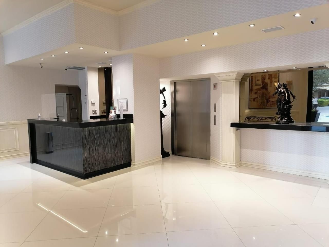 A hotel lobby with a reception desk, a coat check, an elevator, and a statue.