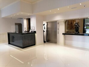 A hotel lobby with a reception desk, a coat check, an elevator, and a statue. - Rose Hotel (Monterrey)