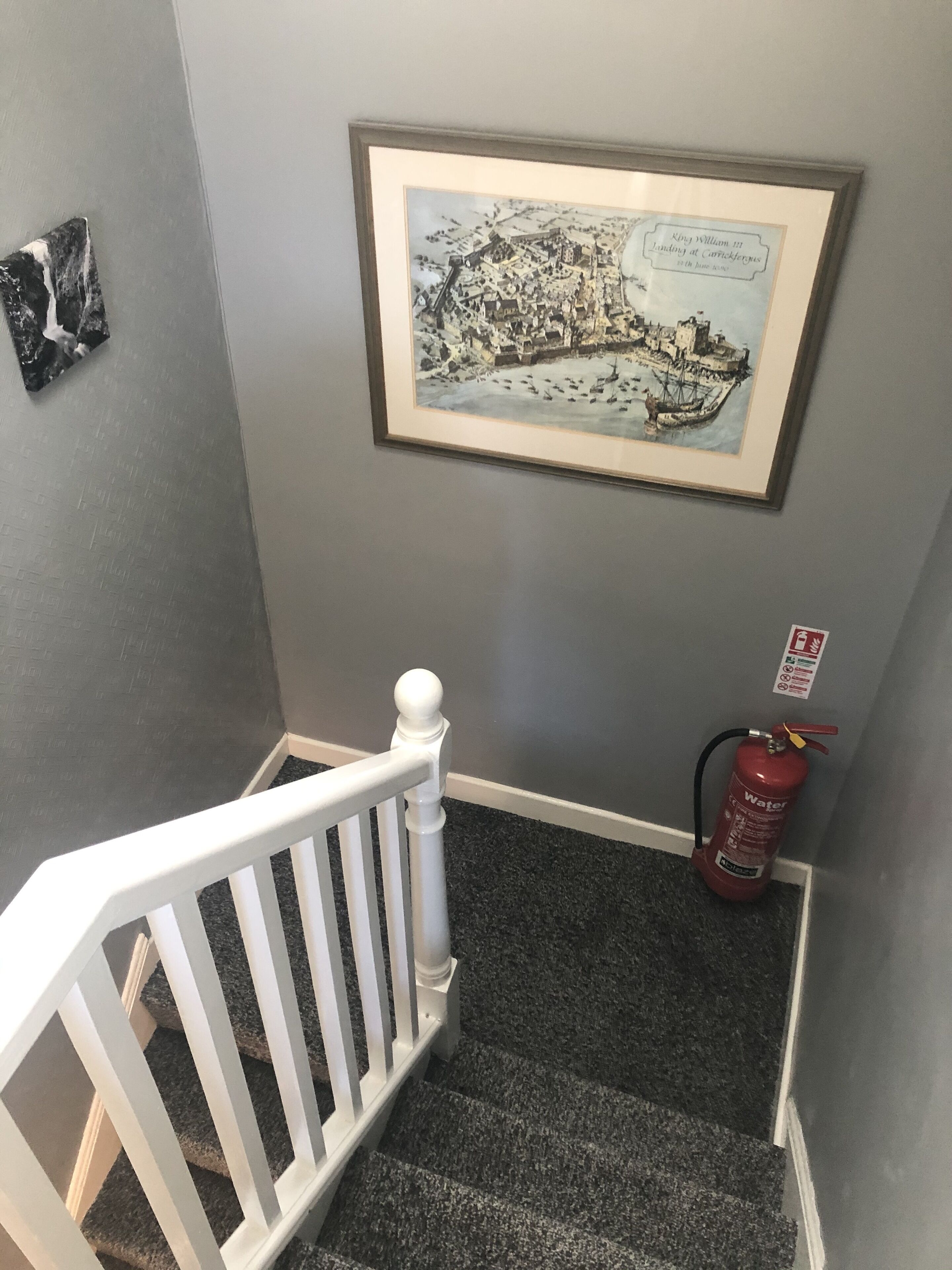 Una escalera con un mapa histórico enmarcado, una barandilla blanca y un extintor en la pared.