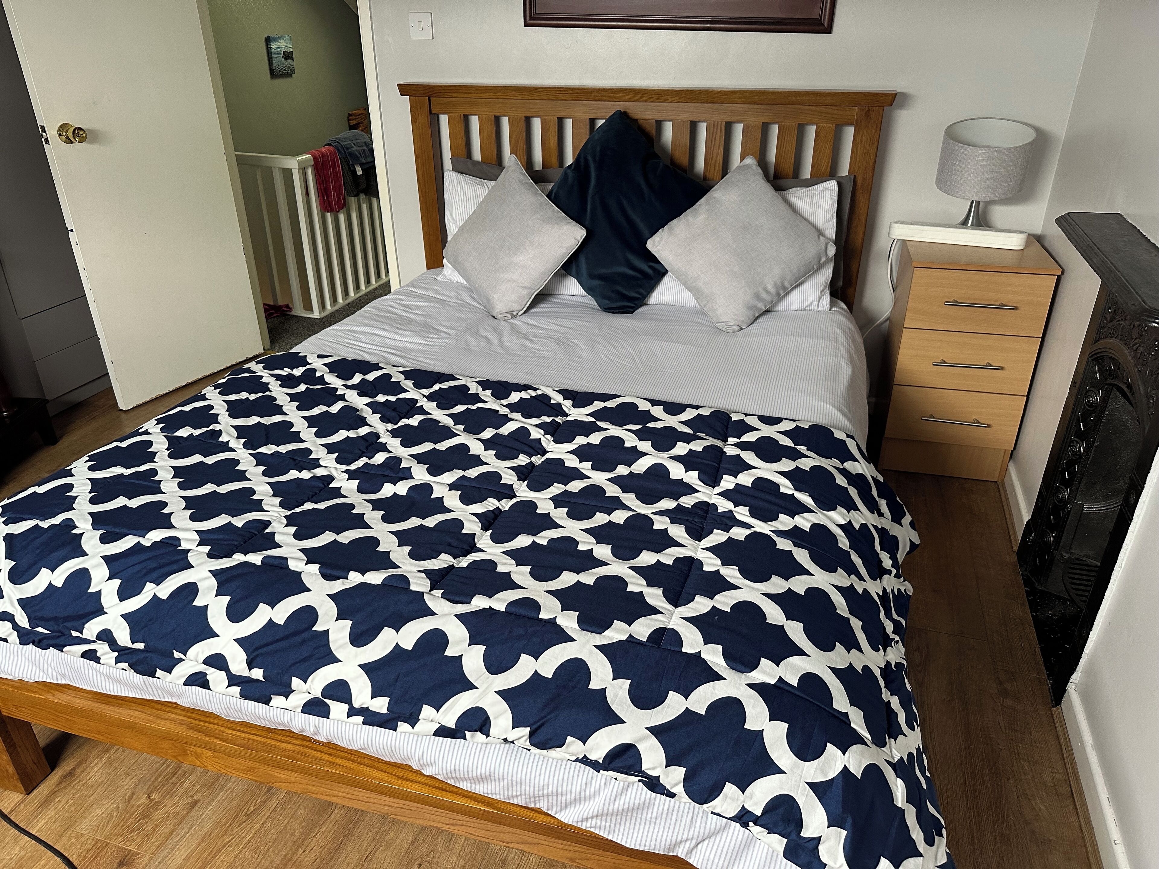 Uma cama bem arrumada com colcha estampada, cabeceira de madeira e mesa de cabeceira com abajur.