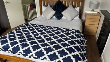 Uma cama bem arrumada com colcha estampada, cabeceira de madeira e mesa de cabeceira com abajur.
