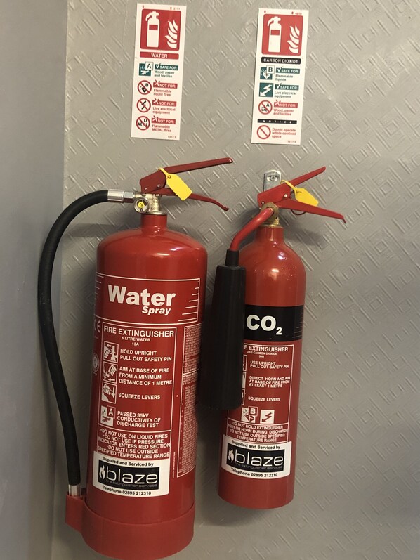 Två brandsläckare monterade på en vägg, varav den ena är märkt med ”Vatten” och den andra med ”CO2”.