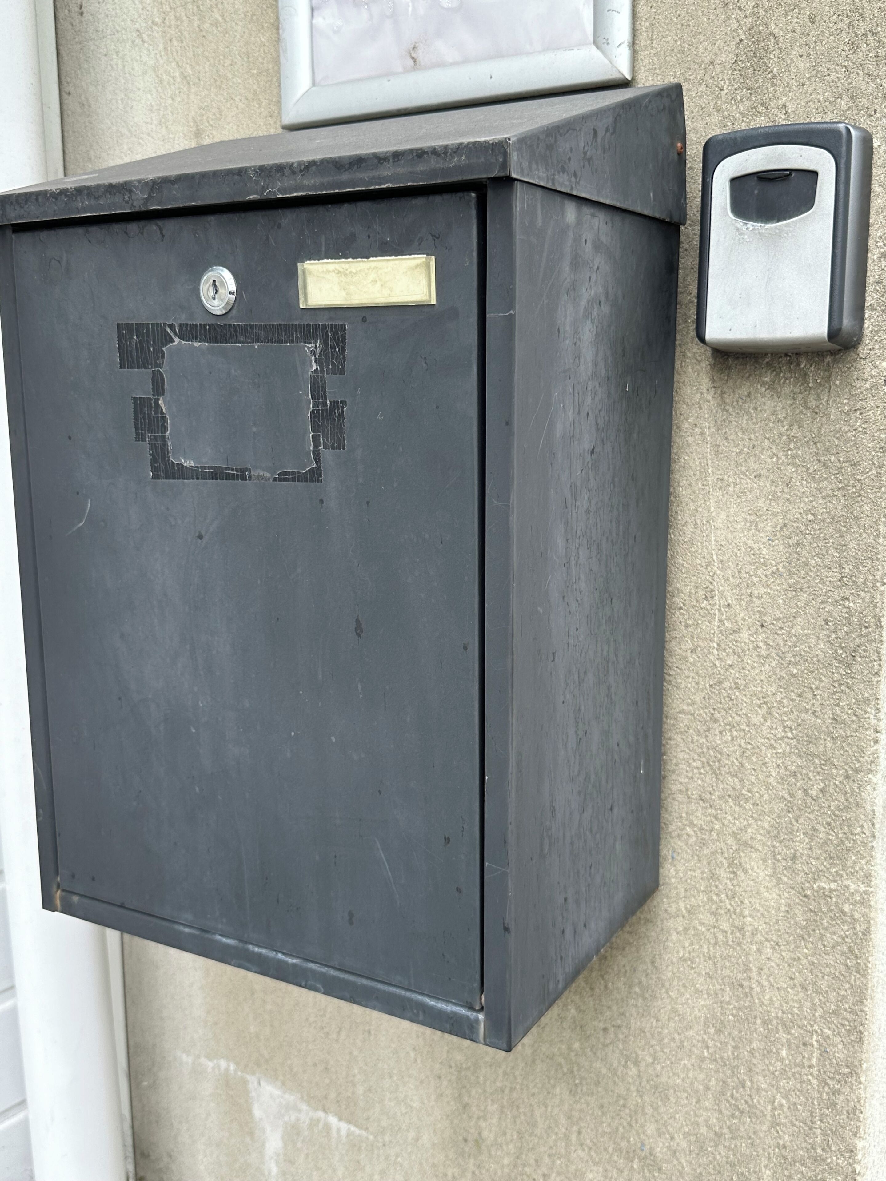 A black metal utility box with a lock and a label, mounted on a textured wall.