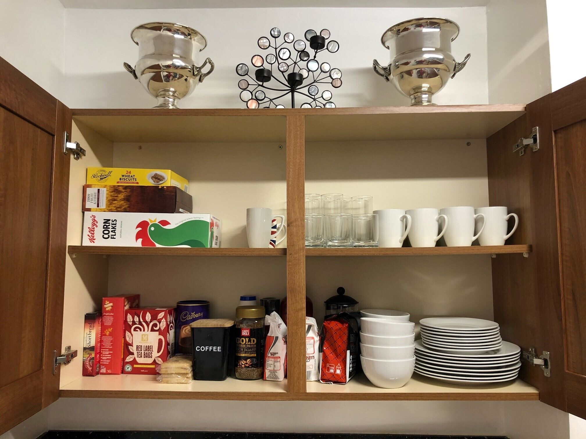 Un armario de cocina con estantes que contienen diversos alimentos, utensilios de cocina y objetos decorativos.