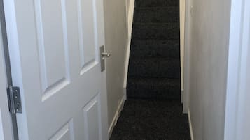 A narrow hallway with a carpeted staircase leading to a landing.