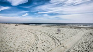 Een zandstrand met sporen van banden en een bord.