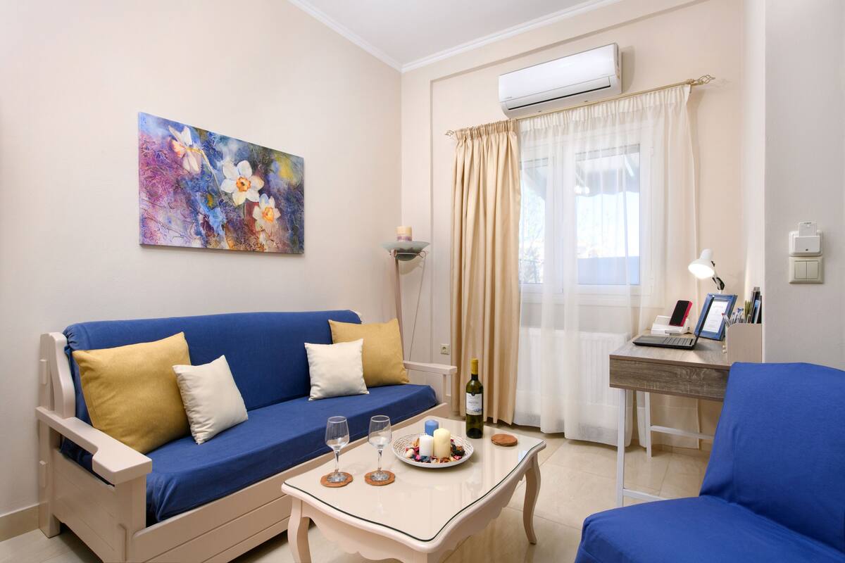 Un salón moderno con un sofá azul, una mesita con una computadora portátil, una botella de vino y dos copas.