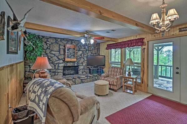 A cozy living room with a stone fireplace, comfortable seating, a television, and a large window offering a view of the outdoors. - Secluded Edgemont Getaway w/ Huge Outdoor Deck! (Edgemont)