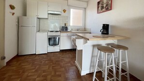 Eine kompakte Küche mit weißen Schränken, einer Mikrowelle, einem Backofen, einer Kaffeemaschine und einem Fenster.