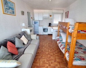 A compact living space with a sofa, a bunk bed, a kitchenette, and a dining area. - GRAND STUDIO FACE A LA PLAGE DU MÔLE (LE CAP D AGDE)