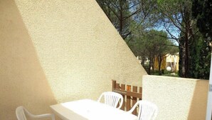 Un patio exterior con una mesa y sillas blancas, una valla de madera y vistas a árboles y edificios al fondo.