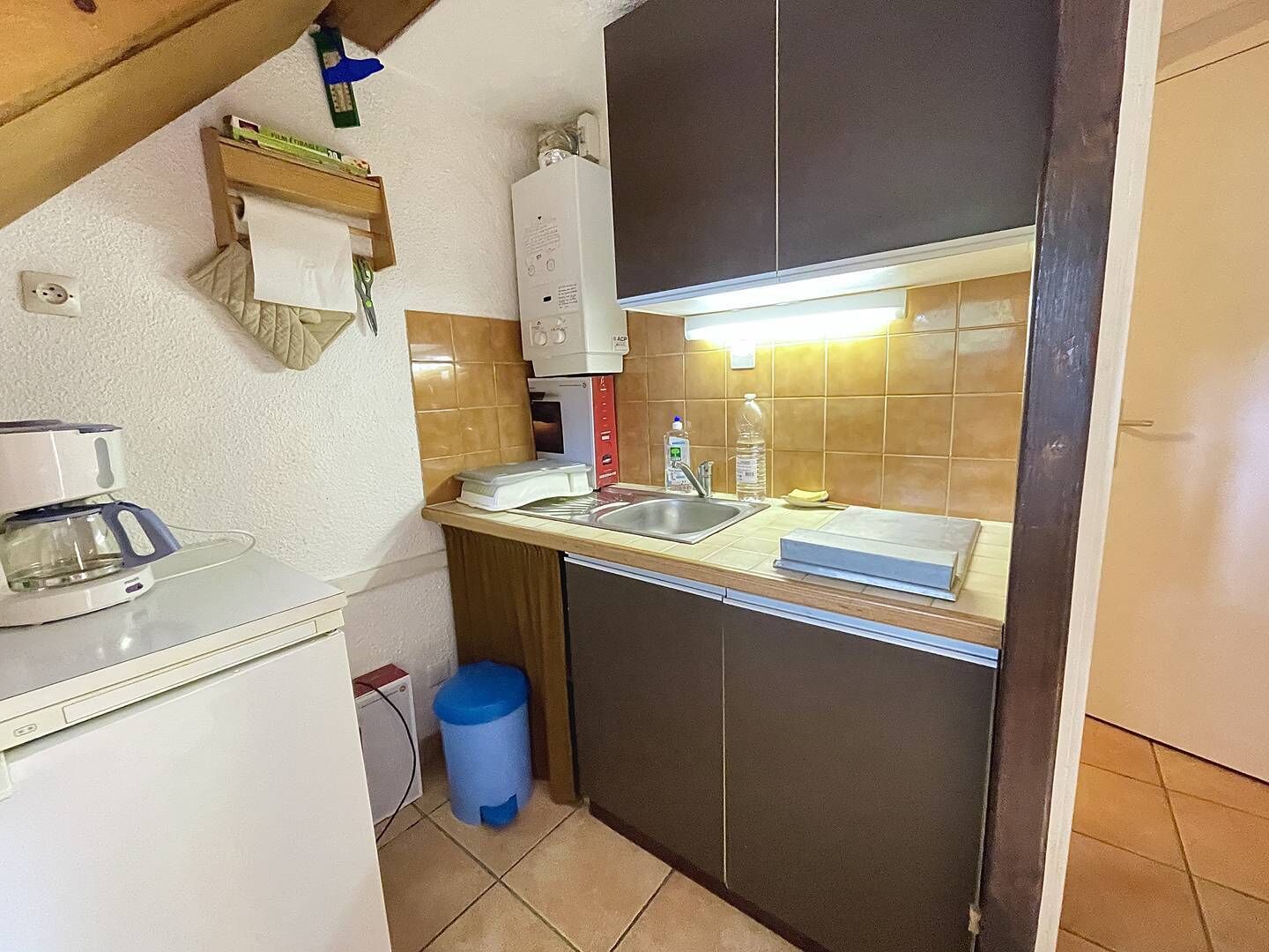 Een kleine keuken met een spoelbak, een koffiezetapparaat en een prullenbak.
