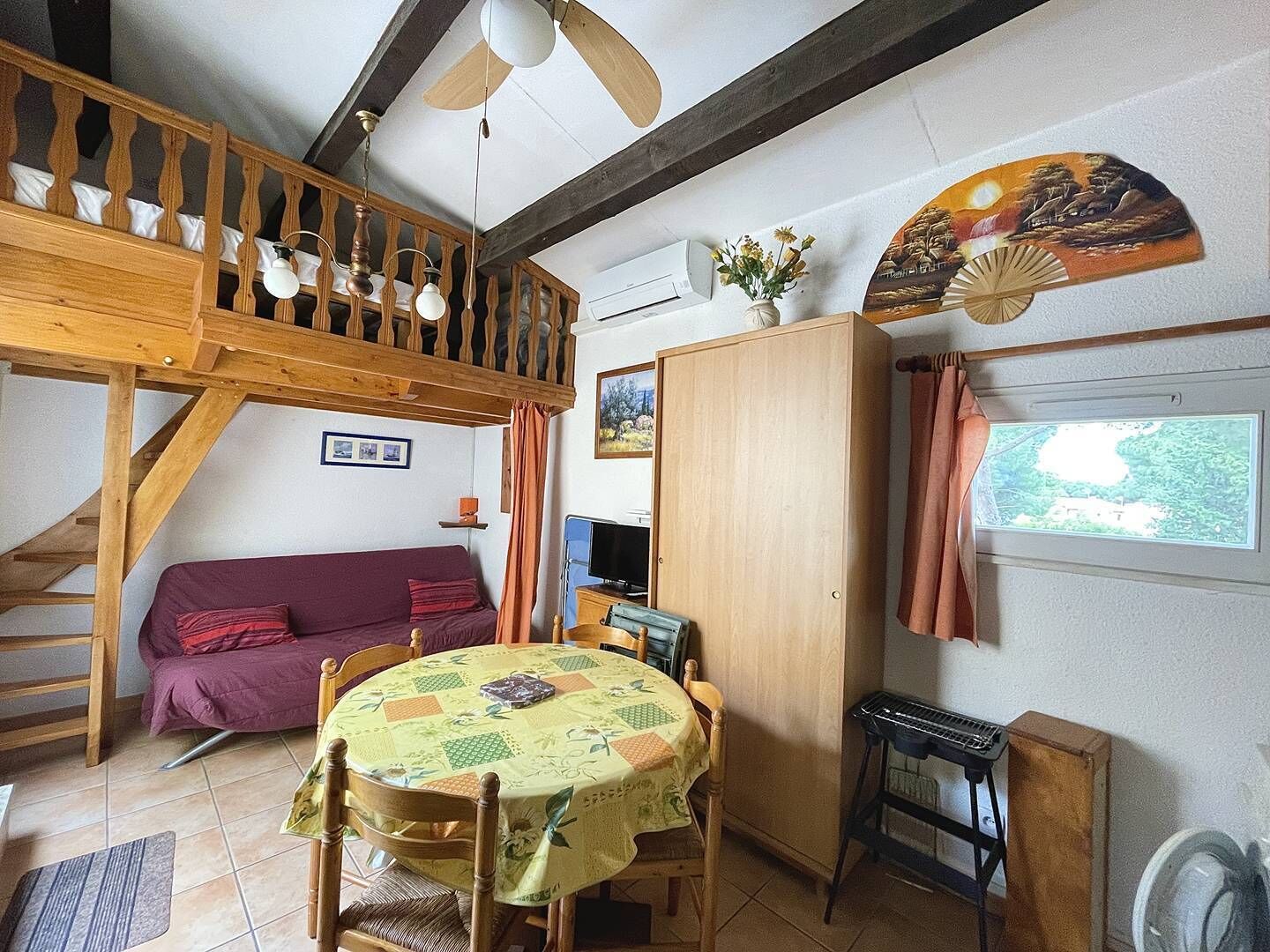 A cozy room with a wooden loft bed, a sofa, a dining table, and a TV.