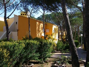 A yellow building with a staircase, surrounded by trees and shrubs.
