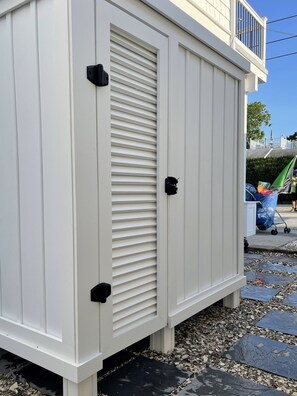 Un edifici blanc amb una persiana tancada, un petit balcó i una zona pavimentada amb fulles disperses.