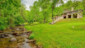 A rustic stone building with a stone staircase leading up to a wooden deck. - Orchard House - creekfront with outdoor fireplace, hot tub, hiking on site (Banner Elk)