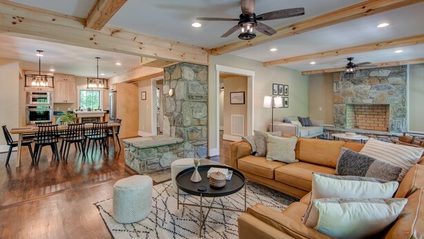 A spacious living area with a stone fireplace, a dining area with wooden furniture, and a kitchen with modern appliances. - Orchard House - creekfront with outdoor fireplace, hot tub, hiking on site (Banner Elk)