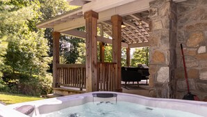 A hot tub under a wooden pergola with a stone wall backdrop. - Orchard House - creekfront with outdoor fireplace, hot tub, hiking on site (Banner Elk)