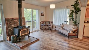 Een gezellige woonkamer met een open haard, een bank, een eettafel met stoelen en een groot raam.