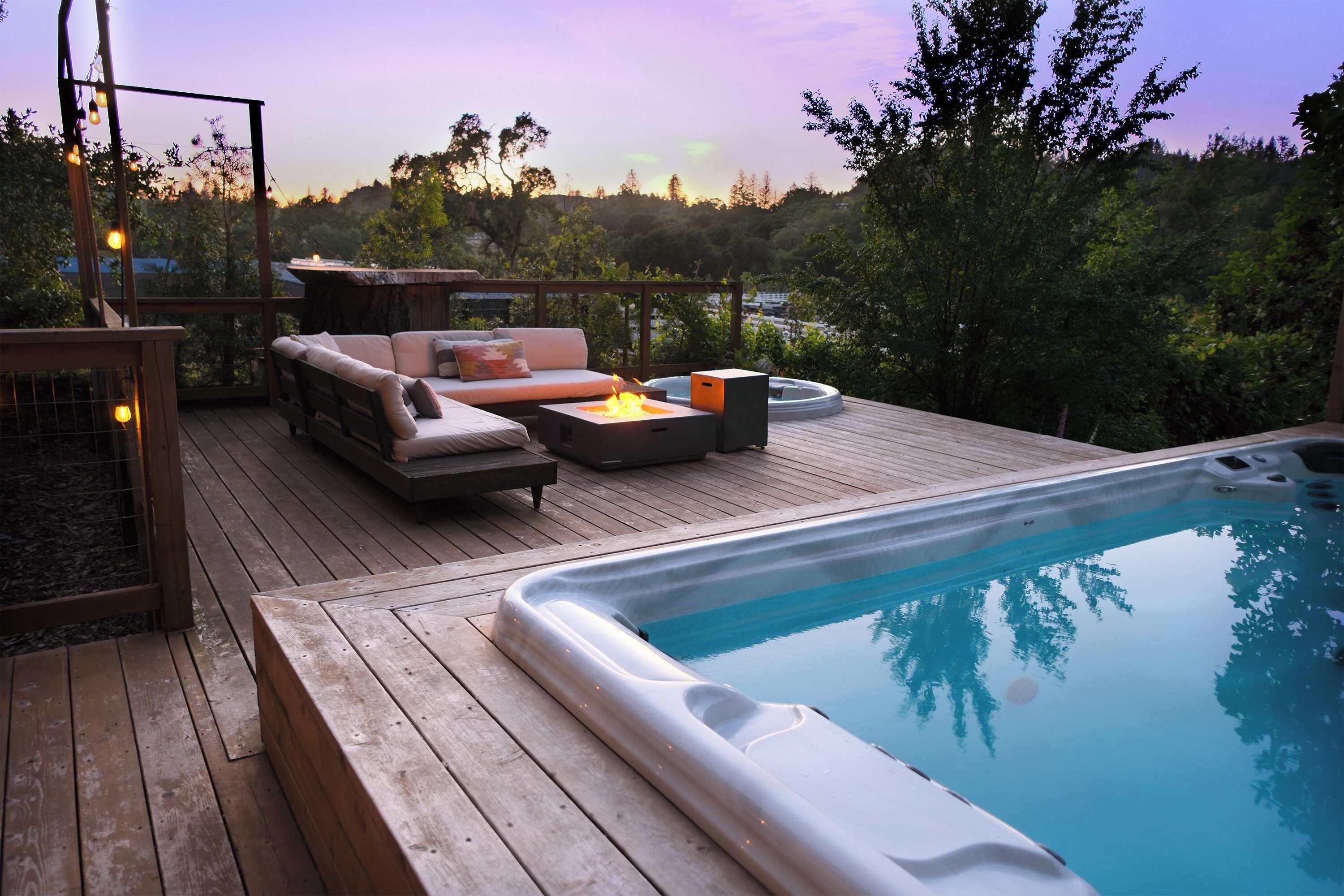 A wooden deck with a hot tub, outdoor seating, and a view of the surrounding trees.