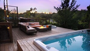 A wooden deck with a hot tub, outdoor seating, and a view of the surrounding trees.
