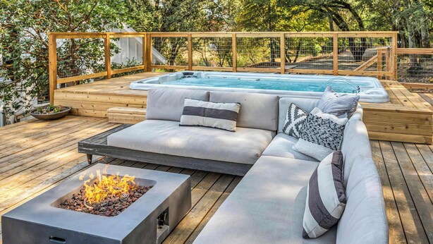 A wooden deck with a hot tub, a fire pit, and a sofa with cushions.