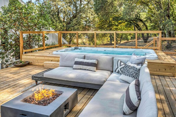 A wooden deck with a hot tub, a fire pit, and a sofa with cushions.