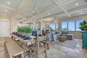 A spacious living area with a wooden dining table, a sofa, and a large window offering a view of the outdoors. - New Ocean View Beach House with a Heated Private Pool! Park Here Walk Everywhere (Cocoa Beach)