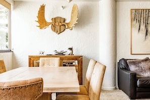 Un coin repas avec une table et des chaises en bois, une tête d’animal empaillée accrochée au mur et un tableau encadré.