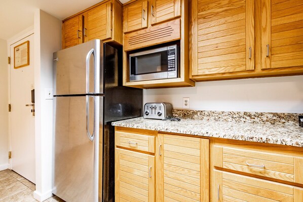 Una cocina con gabinetes de madera, un refrigerador de acero inoxidable, un microondas y un tostador.