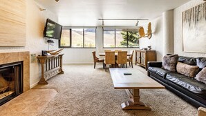 Ein Wohnzimmer mit Kamin, Fernseher, Essbereich mit St ühlen und Tisch sowie einer Couch mit Kissen.