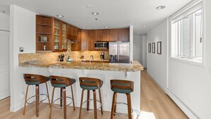 Una cocina moderna con armarios de madera, encimera de granito y refrigerador de acero inoxidable.