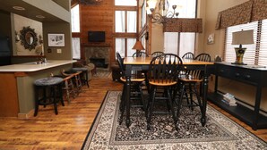Un comedor amplio con una gran mesa de madera y sillas, una barra con taburetes y una chimenea.