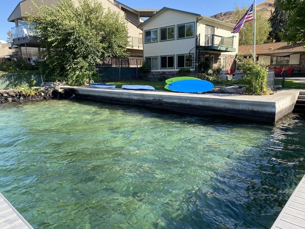 A clear swimming pool with a concrete deck and a small bridge. There are several kayaks and a paddleboard on the deck.