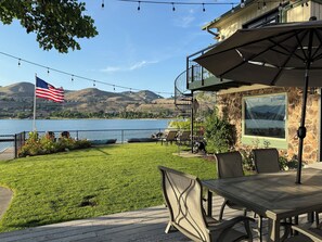 Un patio con una mesa y sillas, con vistas a un lago con barcos y una montaña al fondo.