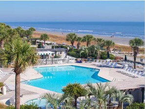 Relax by the pool with ocean views, surrounded by lounge chairs and umbrellas under the shade of palm trees.