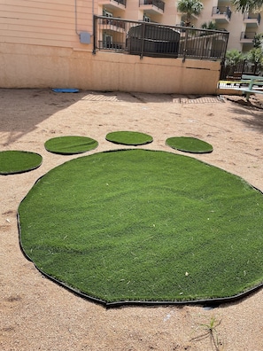 A sandy area with artificial grass paw prints and a metal fence. - Jewell by the Sea, Oceanview, King Size Bed, Dog Friendly! (Galveston)