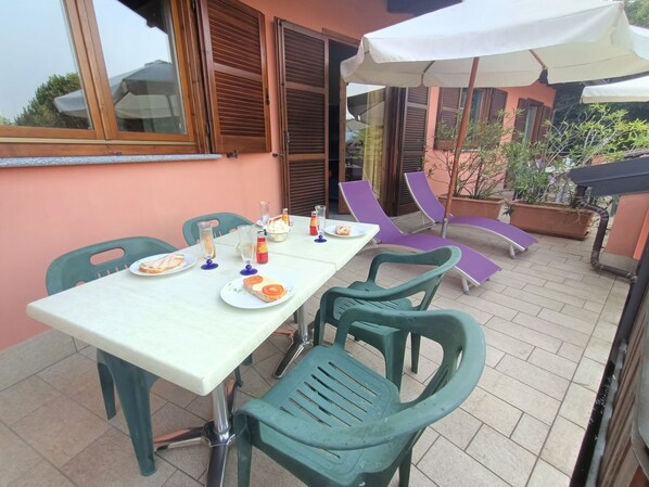 Un área de comedor al aire libre con una mesa lista para dos personas, rodeada de sillas de plástico verde.