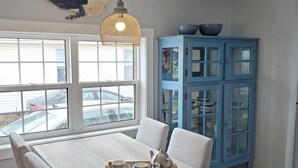 Un coin repas avec une table et des chaises aux couleurs claires, un luminaire suspendu et un buffet bleu avec des portes en verre.