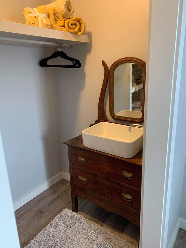 Un baño con tocador de madera, un lavamanos blanco, un espejo y un tapete beige.
