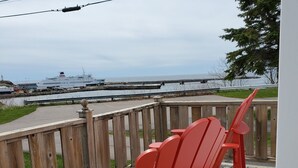 Une terrasse en bois avec des fauteuils Adirondack rouges, donnant sur un paysage marin.