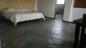 Ein Schlafzimmer mit Steinboden, einem Bett, einer Holztür und einem Fenster.