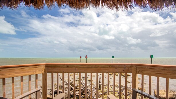 A wooden deck with two chairs overlooking a beach with a clear view of the ocean and distant buoys.