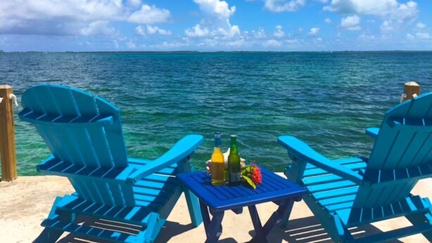 Two blue Adirondack chairs facing a body of water with a clear sky. - Situated on the Ocean Jacaranda Bay Villa  (Nassau)