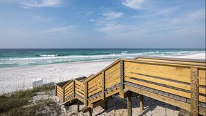 En träpromenad som leder ner till en sandstrand med utsikt över havet.