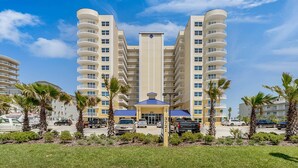 A multi-story hotel with a central atrium, parking area, and palm trees. - Luxury Oceanfront Condo in Daytona Beach Shores with Gorgeous Views! 4BR, 3BA (Daytona Beach Shores)