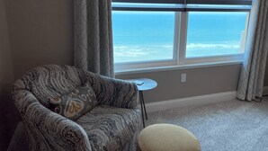 A room with a view of the ocean through large windows, a patterned armchair, a small round table, and a beige ottoman. - Luxury Oceanfront Condo in Daytona Beach Shores with Gorgeous Views! 4BR, 3BA (Daytona Beach Shores)