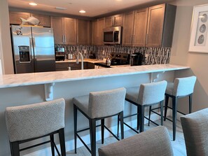 Enjoy cooking and socializing in this stylish kitchen and bar area, featuring a refrigerator, microwave, and wooden cabinets.