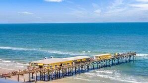 A pier with a yellow building, extending into the ocean. - Luxury Oceanfront Condo in Daytona Beach Shores with Gorgeous Views! 4BR, 3BA (Daytona Beach Shores)